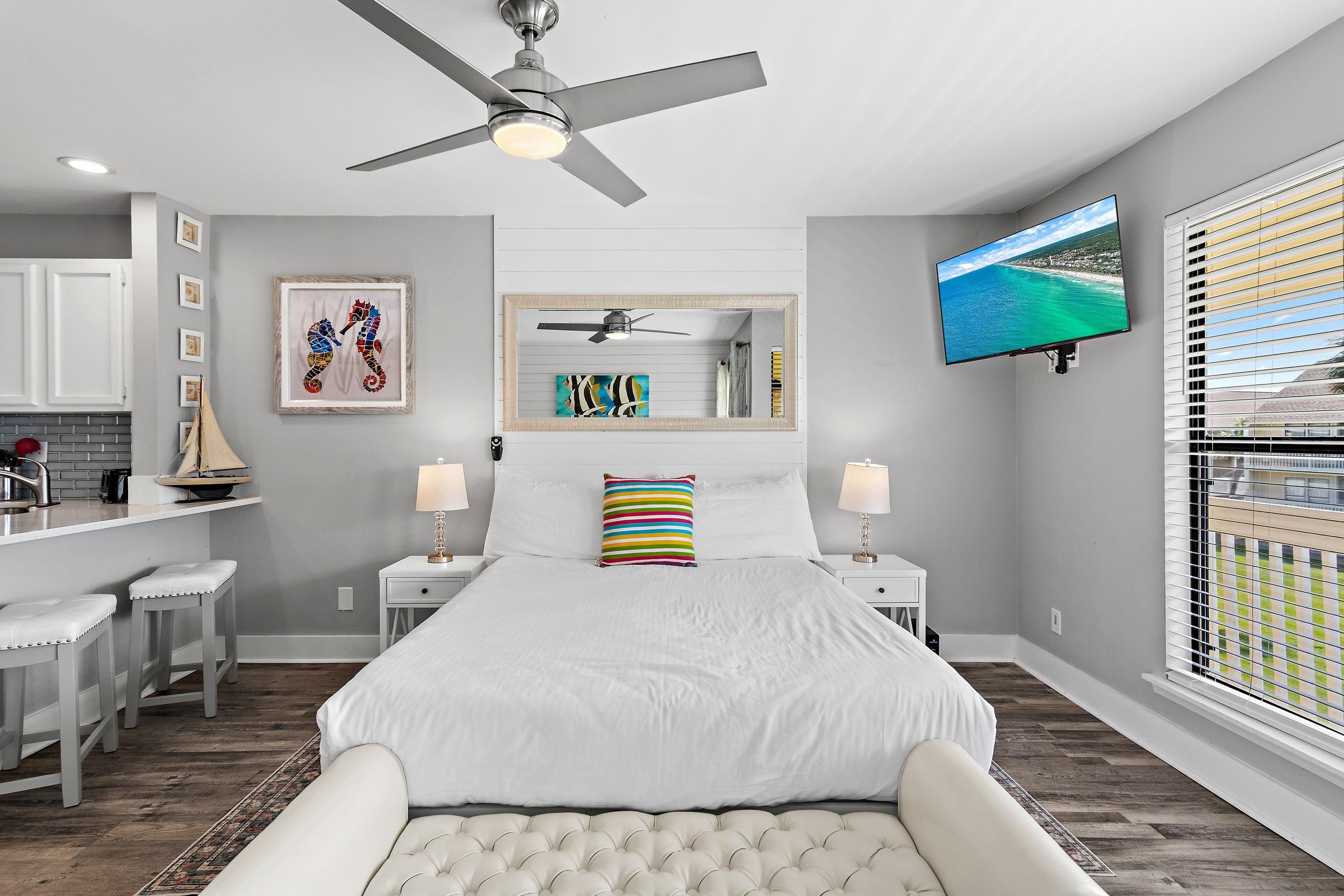 Un dormitorio con cama, ventilador de techo, televisor y vistas al exterior.