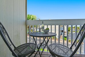 A balcony with two metal chairs, a small round table, a bottle of wine, and a bowl of grapes. - Sandpiper Cove 8246 (Destin)