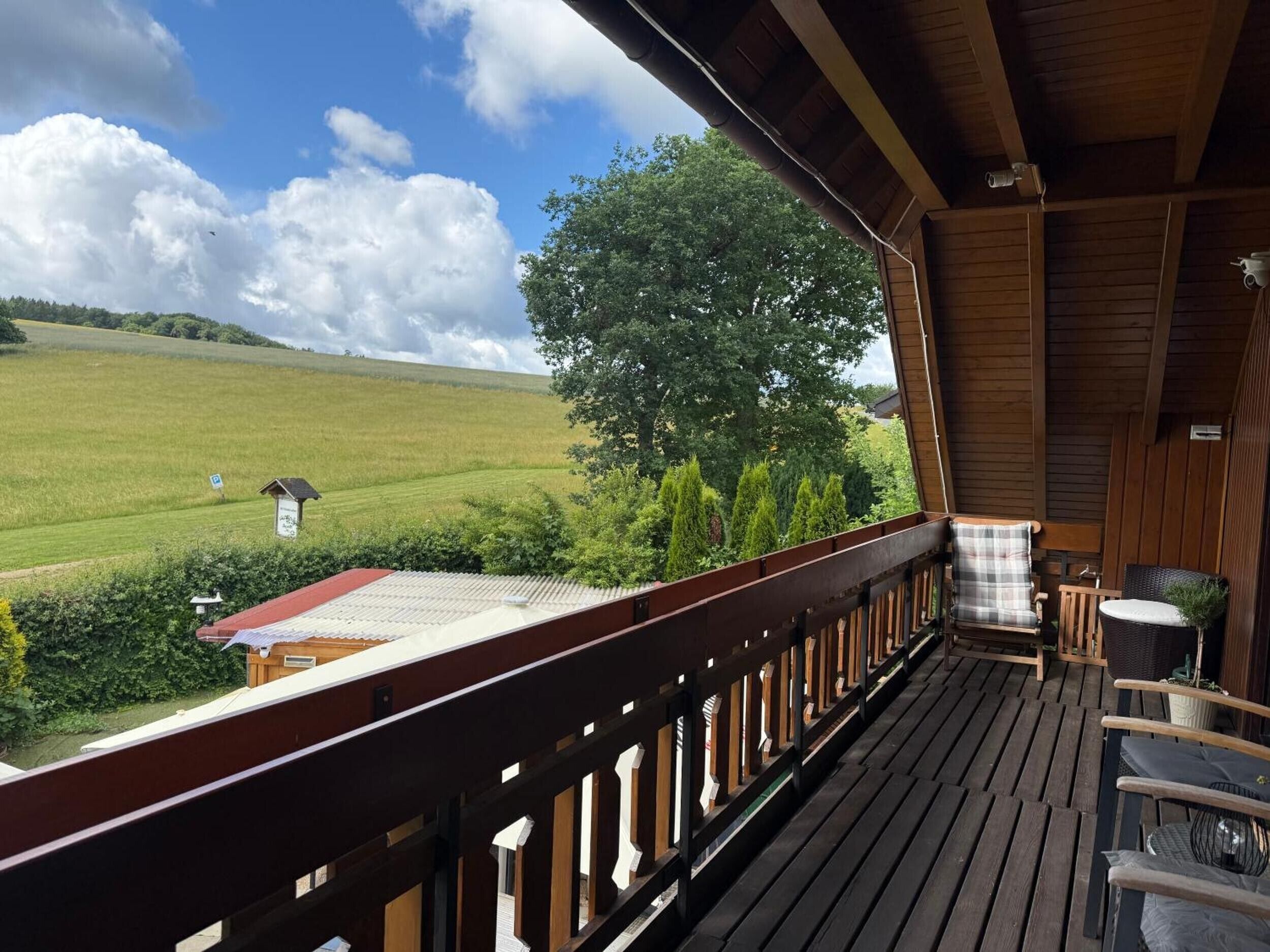 Eine Holzterrasse mit Blick auf ein grünes Feld und einen Baum.