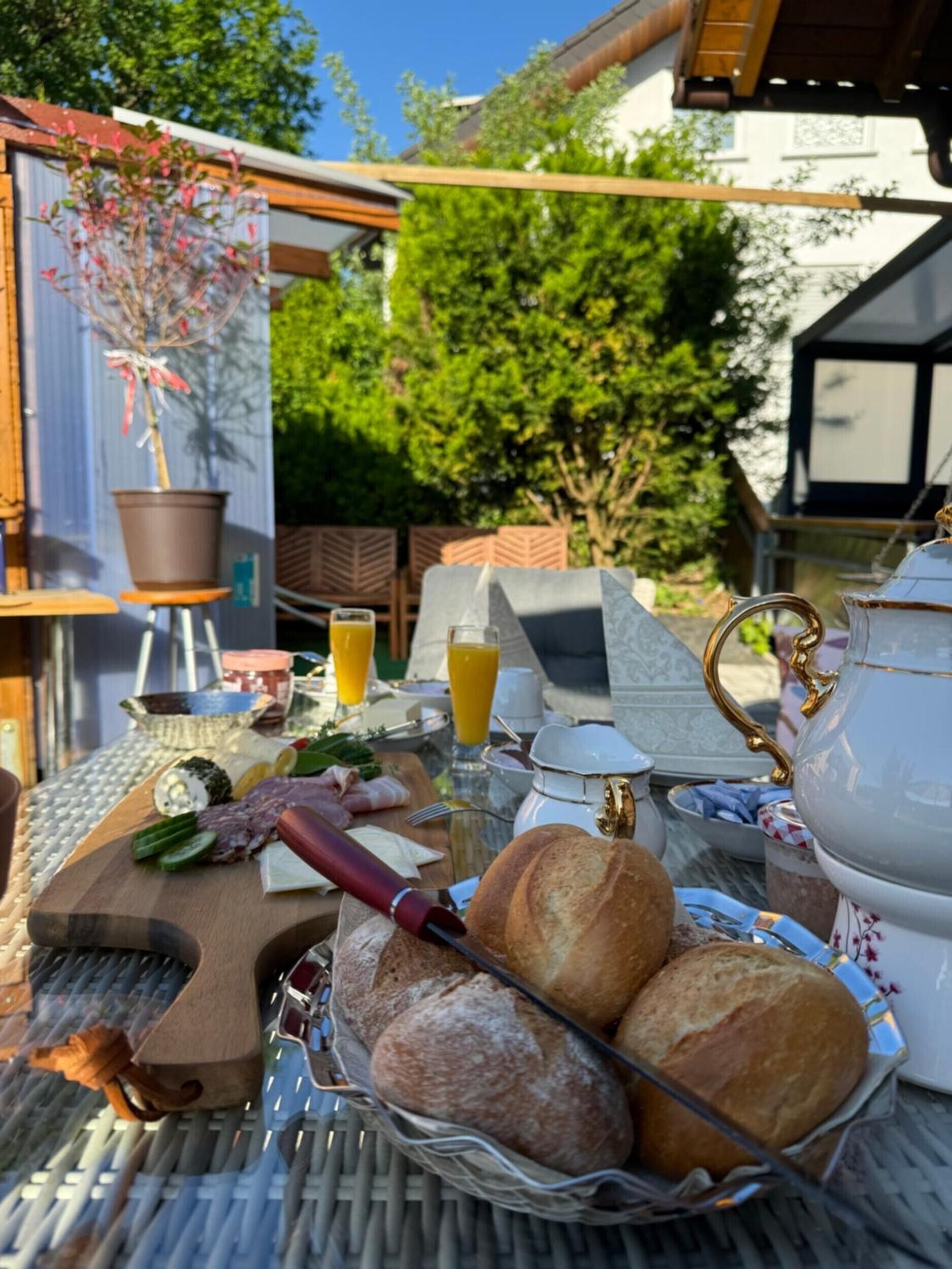 En frukostuppsättning med bröd, ost och en dryck på ett utomhusbord.