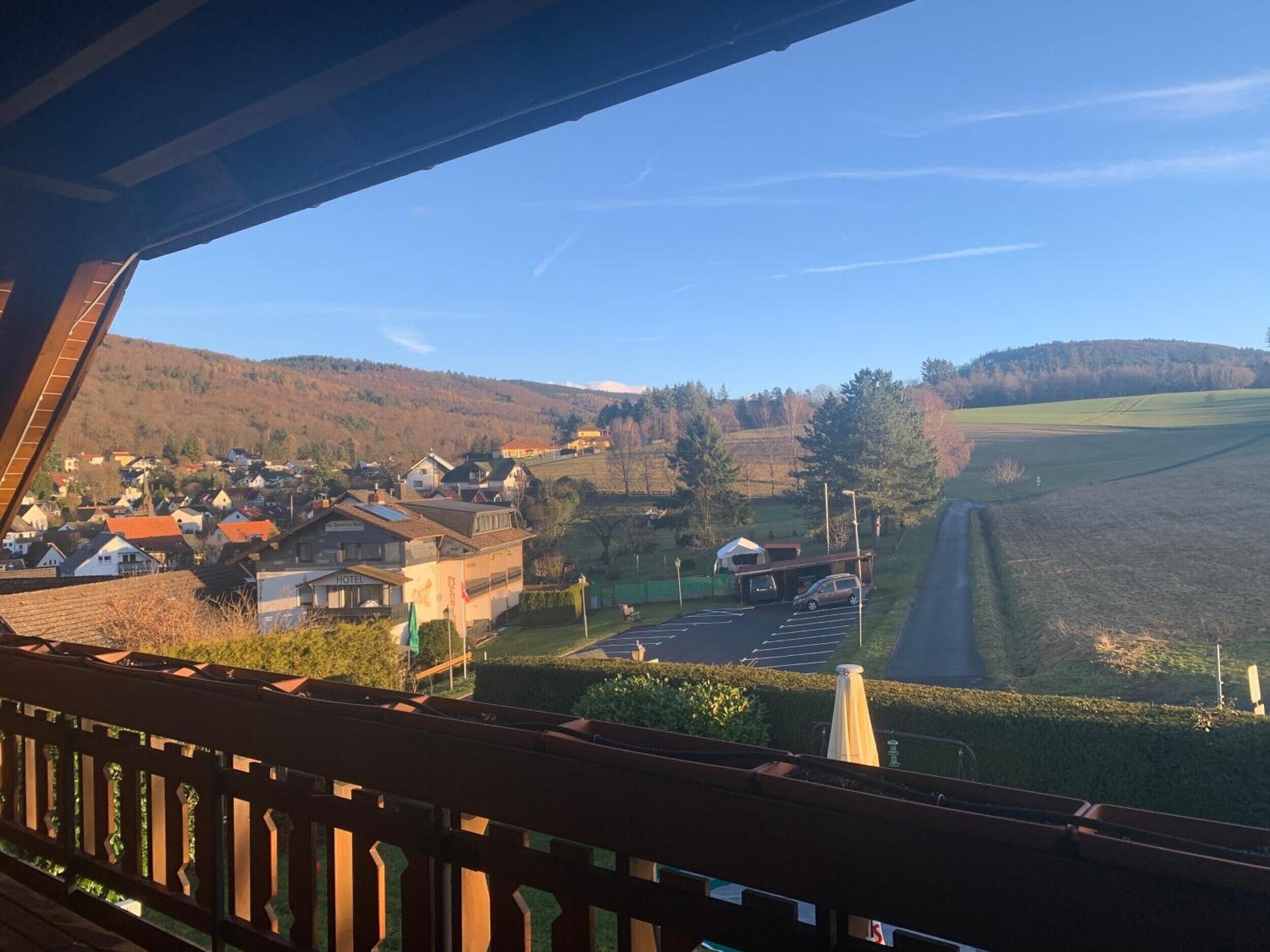 Vista desde un balcón sobre un pueblo con un hotel, un estacionamiento y una carretera que sube a una colina.
