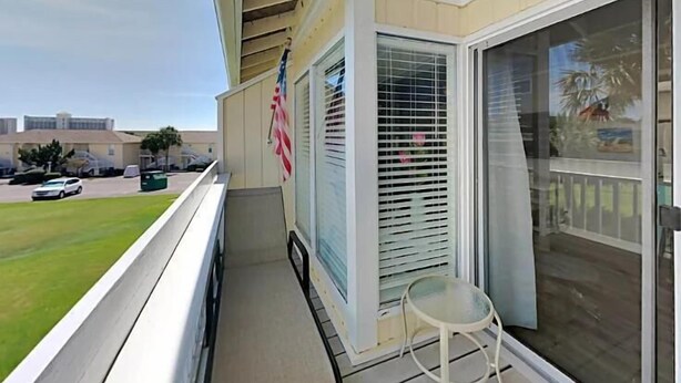Uma varanda com vista para um estacionamento e edifícios, uma pequena mesa e uma bandeira americana.