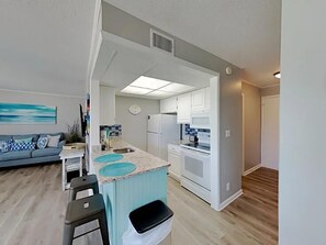 A modern kitchen with white cabinets, a central island, and a dining area with bar stools. - Sandpiper Cove 2015 (Destin)