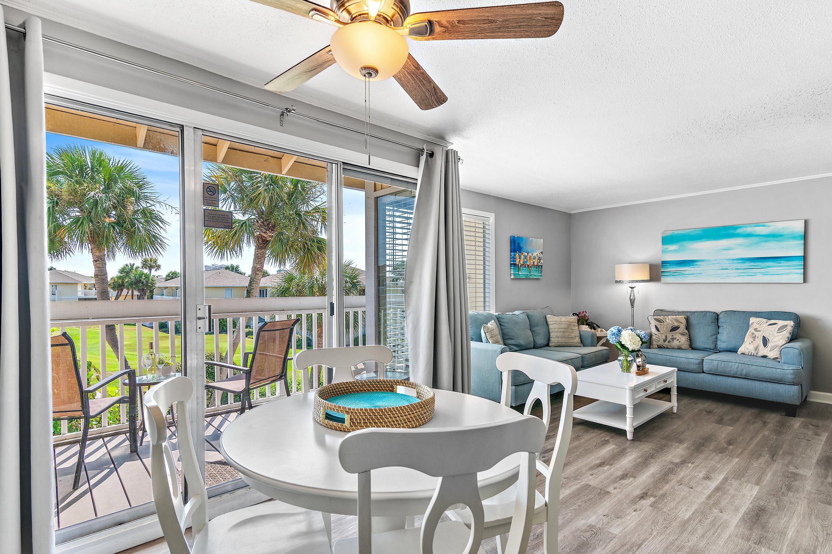 A spacious living area with a balcony, a ceiling fan, and a view of palm trees.