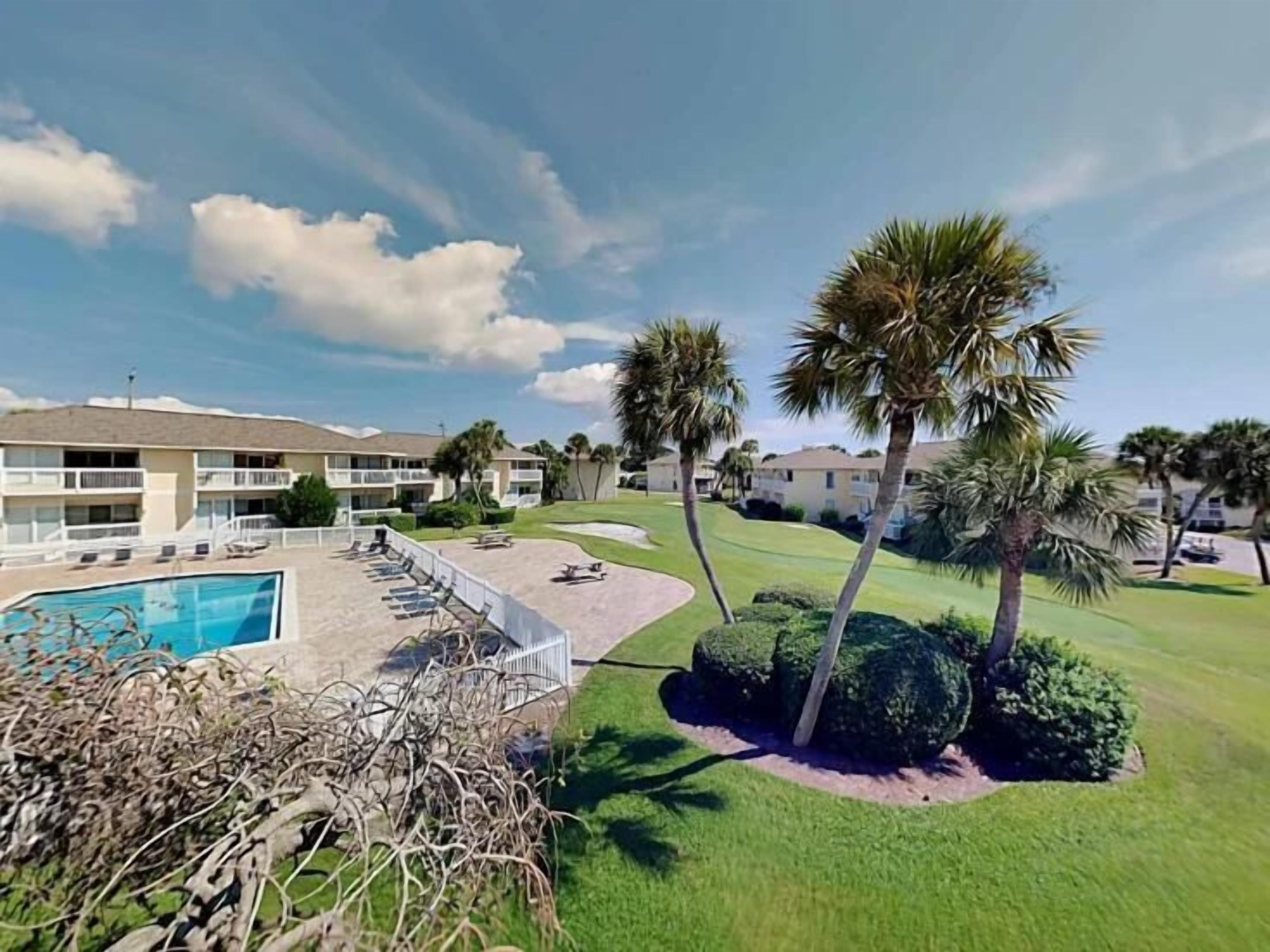 Un hotel con piscina, palmeras y un césped cuidado.