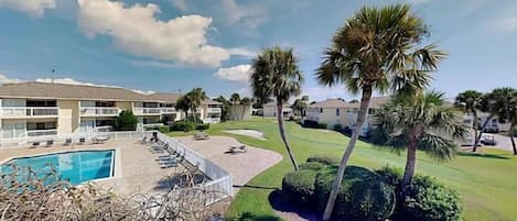 Un hotel con piscina, palmeras y un césped cuidado.