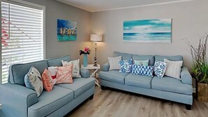 Uma sala de estar com dois sofás, uma luminária e obras de arte nas paredes.