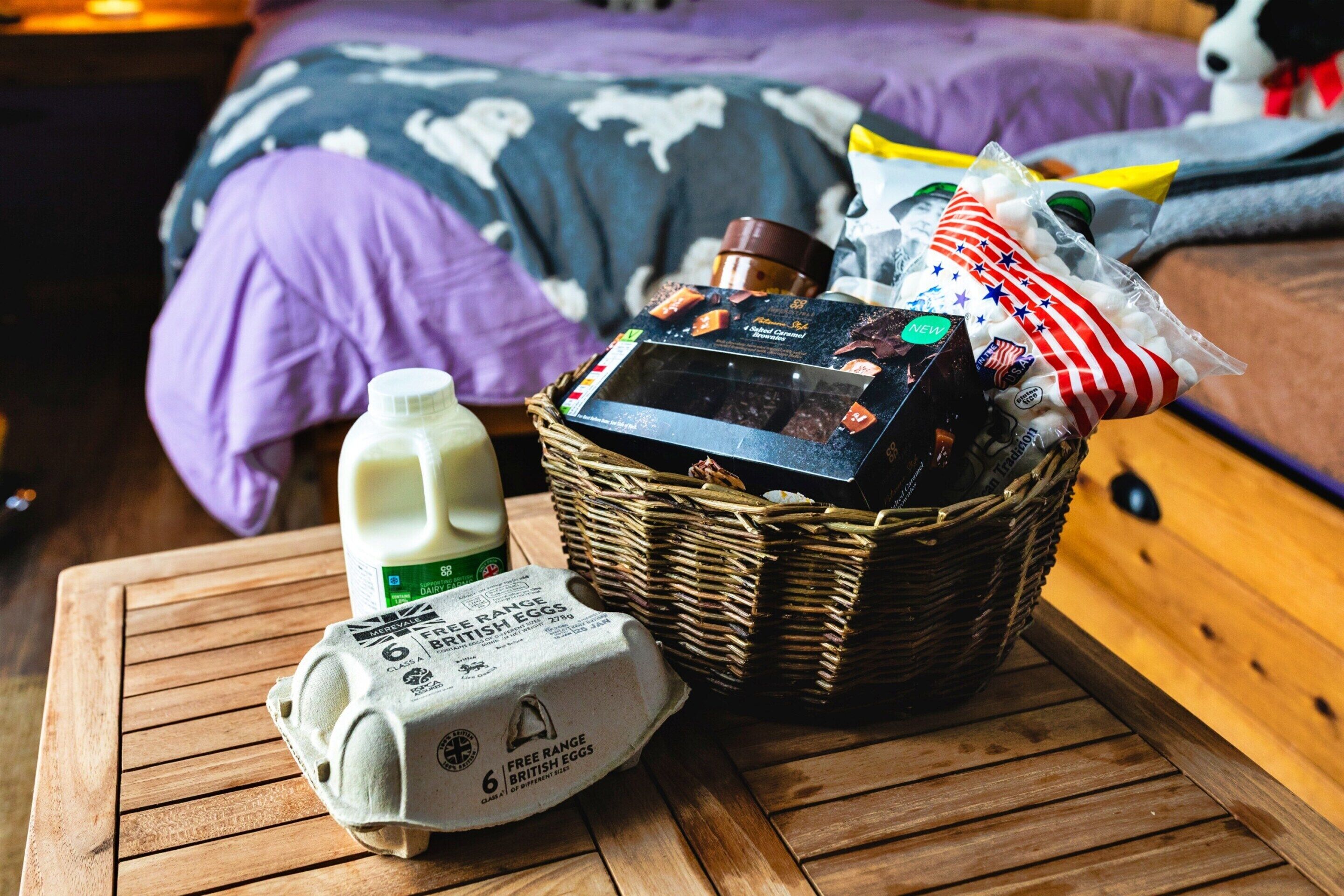 Ein Korb mit verschiedenen Artikeln, eine Milchkarton und eine Eierpackung auf einem Holztisch.