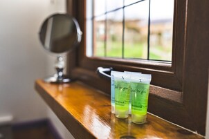 Un baño con tocador de madera, un espejo y tres botellas verdes de champú y acondicionador sobre el mostrador.