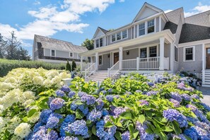 A two-story house with a porch and a garden with hydrangeas. - Elevated Osterville Escape with Heated Pool RPAM128 (Osterville)