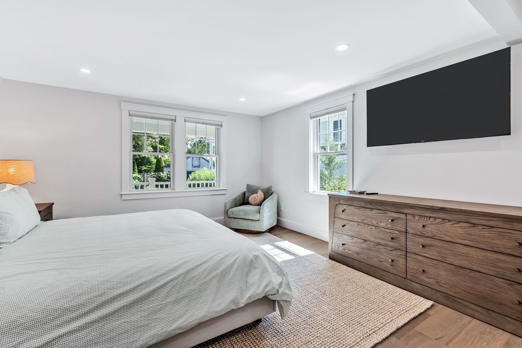 A bedroom with a bed, a chair, a TV, and a wooden dresser.