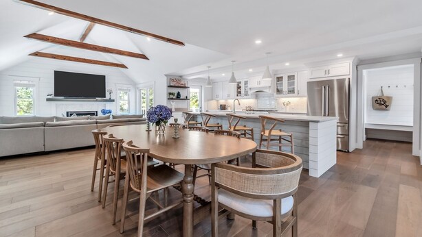 Una cocina moderna con armarios blancos, una isla central y un comedor con sillas de madera.