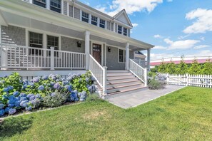 A two-story house with a front porch, a white picket fence, and a well-maintained lawn. - Elevated Osterville Escape with Heated Pool RPAM128 (Osterville)