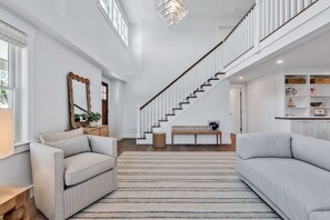 A spacious living area with a staircase, a sofa, a bench, and a decorative mirror. - Elevated Osterville Escape with Heated Pool RPAM128 (Osterville)