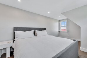 A bedroom with a bed, bedside table, and a window with shutters. - Elevated Osterville Escape with Heated Pool RPAM128 (Osterville)