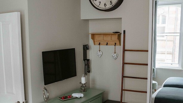 Une chambre à coucher comprenant un lit, une commode, une horloge murale, un téléviseur et une fenêtre.