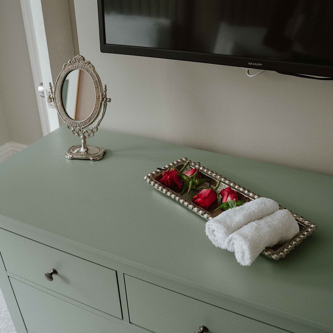 Een groene wastafel met spiegel, een dienblad met rode rozen en een opgevouwen witte handdoek.