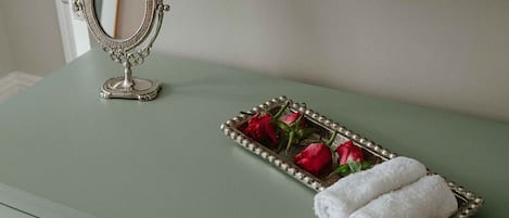 A green vanity with a mirror, a tray with red roses, and a folded white towel.