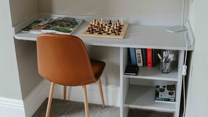 Un espace de travail comprenant un bureau, une chaise, un jeu d’échecs, une lampe et des étagères.