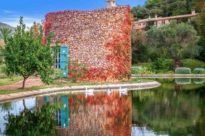 A stone building with a reflection in a pond, surrounded by greenery and a clear sky. - The Dream Valley of Mallorca (Pollença)