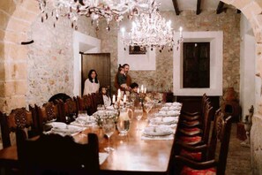 Una larga mesa de comedor lista para una comida, con velas y rodeada de sillas de madera.