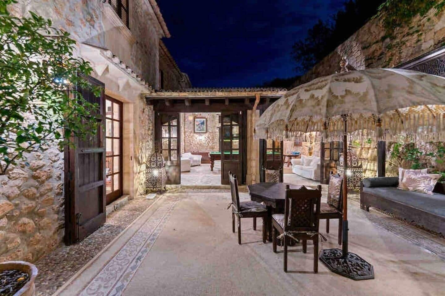 An outdoor patio with stone walls, a dining table, chairs, and a large umbrella.