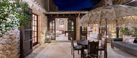 An outdoor patio with stone walls, a dining table, chairs, and a large umbrella.