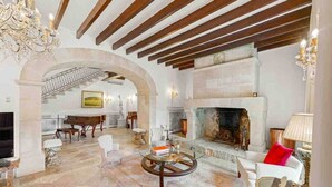 A spacious living room with a fireplace, a grand piano, and a chandelier. - The Dream Valley of Mallorca (Pollença)