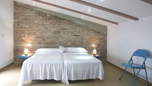 A bedroom with a double bed, two bedside tables with lamps, a blue chair, and exposed brick walls. - Beachfront villa in Valencia for up to 25 people. (València)