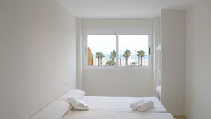 A bedroom with a large bed, white bedding, and a window with a view of palm trees and the sea. - Beachfront villa in Valencia for up to 25 people. (València)