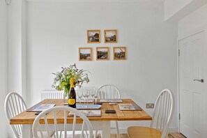 Ein Essbereich mit einem Holztisch, weißen Stühlen, einer Blumenvase und sechs gerahmten Bildern an der Wand.