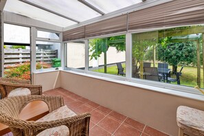 A covered patio with wicker furniture, large windows, and a view of a garden. - Anglesey Country Retreat (Amlwch)