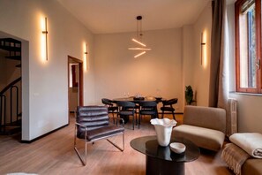 A modern living room with a dining area, featuring a staircase, leather armchair, round coffee table, and pendant lighting. - Trastevere 5BR Estate: Cinema, Jacuzzi & Terrace (Roma)
