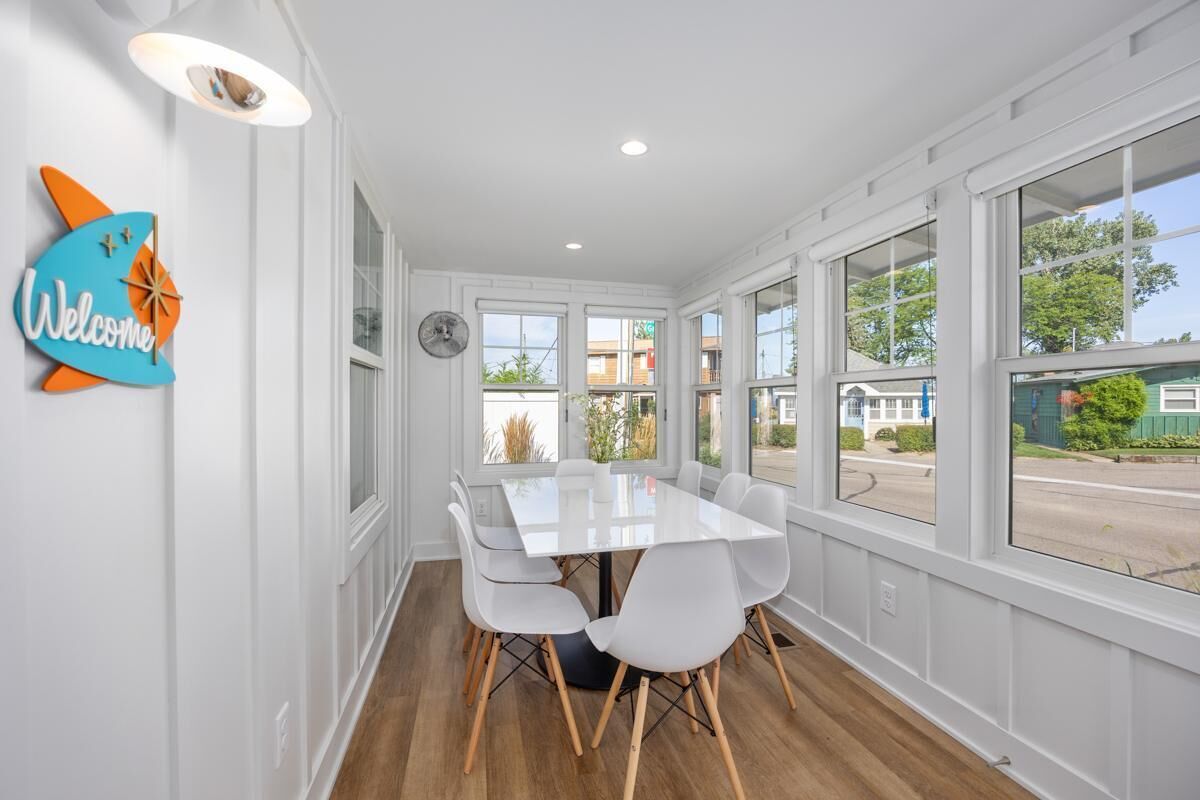 A modern dining area with a white table and chairs, large windows, and a 'Welcome' sign.