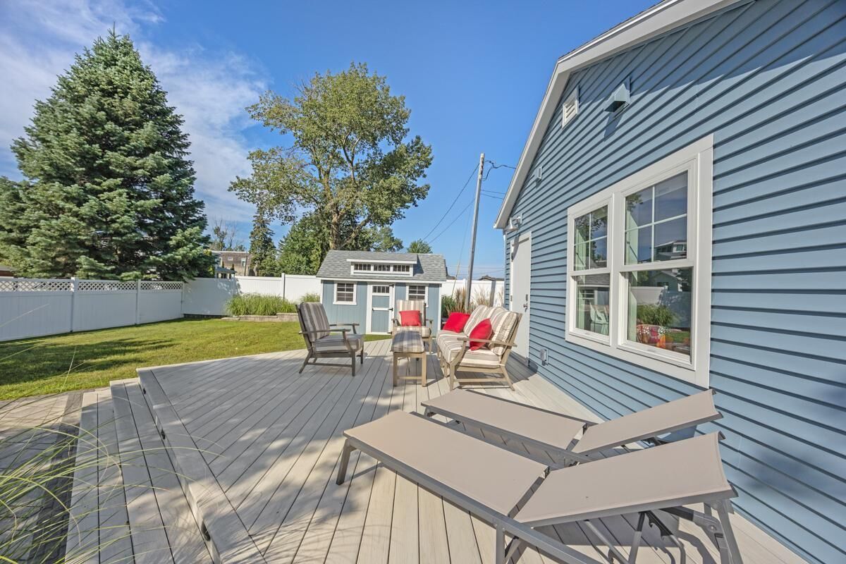 A deck with outdoor furniture, a house with blue siding, and a large evergreen tree.