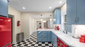 Una cocina moderna con piso a cuadros, armarios azules, un refrigerador rojo y luces colgantes.