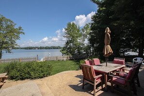 An outdoor patio with a table and chairs, a wooden fence, and a view of a lake. - Bluegill Hill (Fennville)