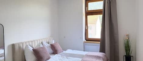 A bedroom with a bed, bedside table, and a window with curtains.