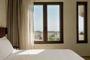 Ein Hotelzimmer mit Bett, Fenster und Blick auf eine Stadtlandschaft, sowie einem Vorhang.