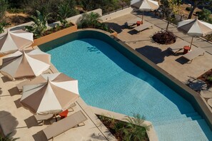 A swimming pool with sun loungers and umbrellas, surrounded by a landscaped area with plants and a view of the surrounding landscape. - Linum Hill Elegant 2BR Apt with Sea View & Pool (Agios Nikolaos)