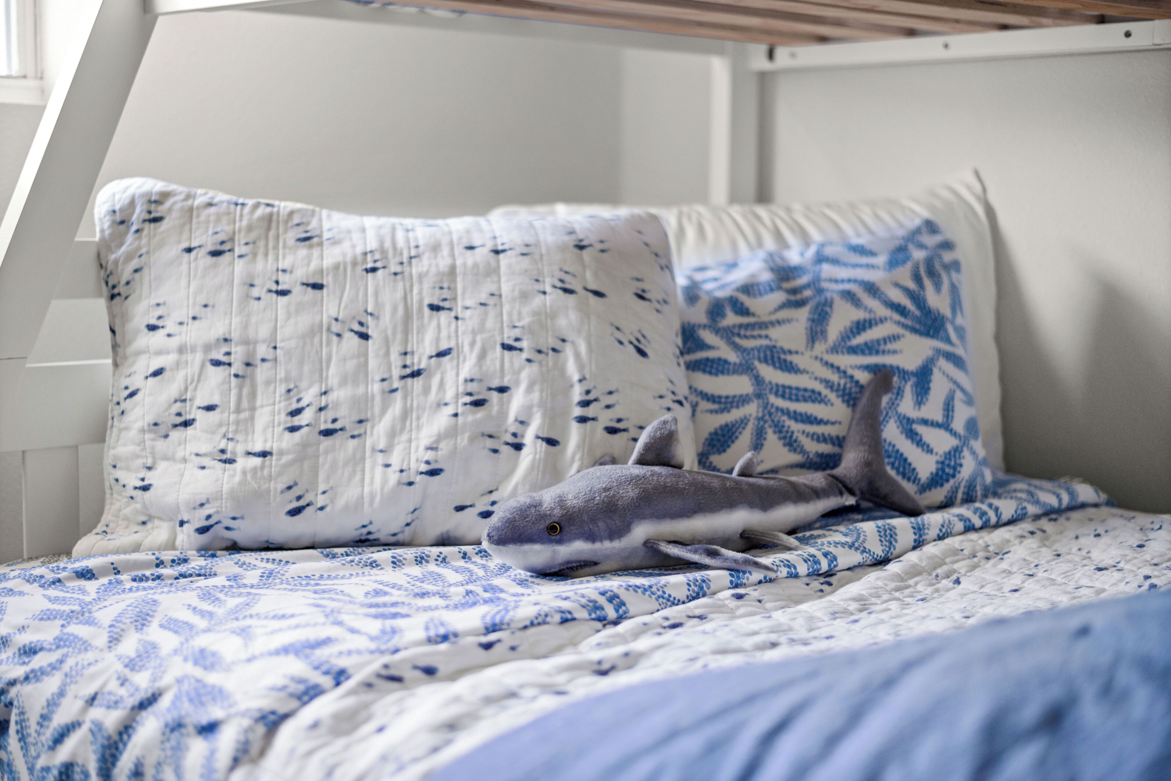A bed with a patterned blue and white bedding, a pillow with a leaf design, and a plush shark toy.