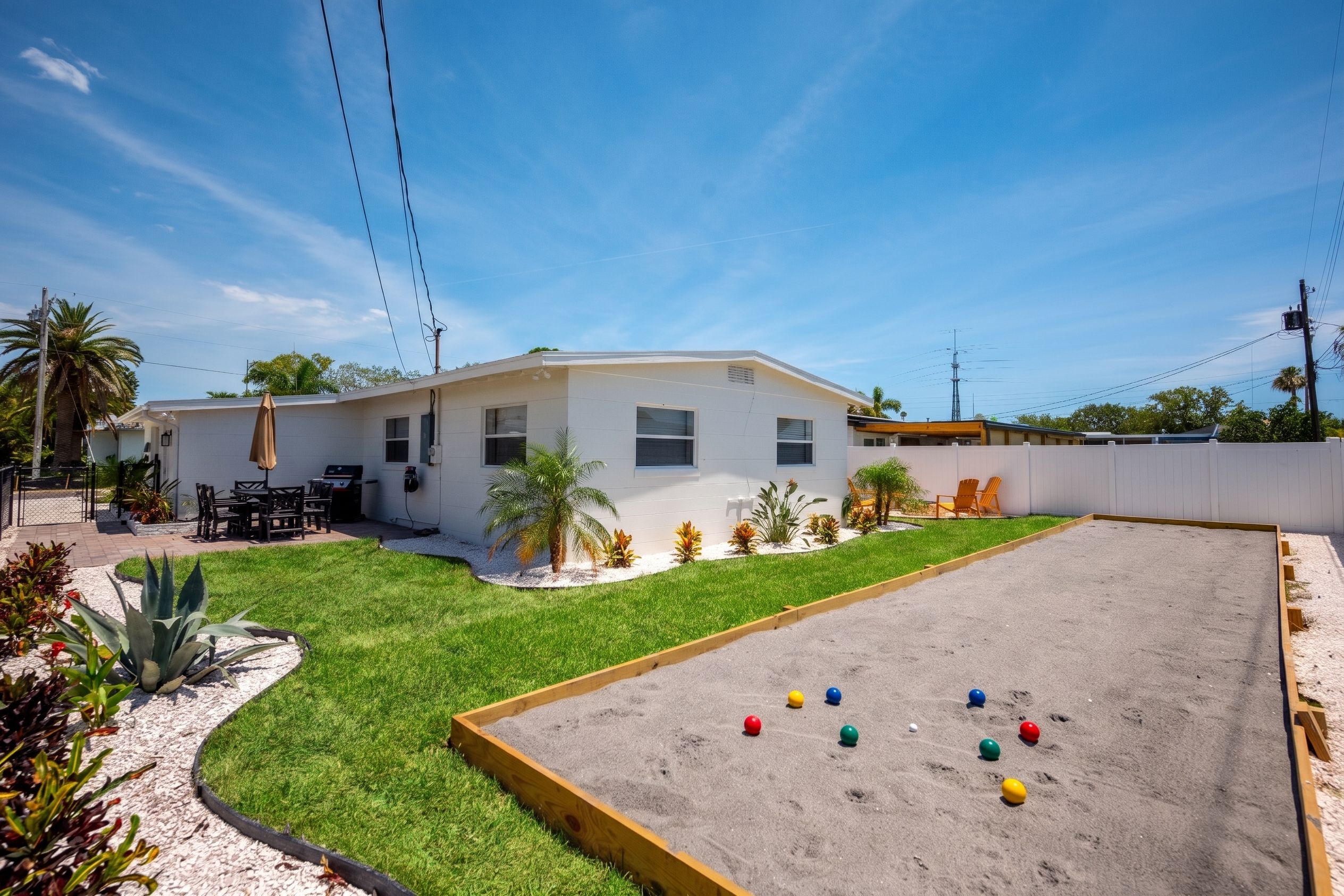 A residential property with a fenced backyard, a patio with outdoor furniture, and a sandpit with colorful balls.