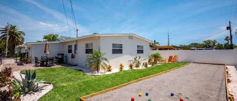 A residential property with a fenced backyard, a patio with outdoor furniture, and a sandpit with colorful balls.