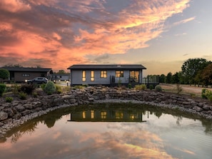 A modern house with a stone wall and a pond in front. - Resort Chalet Near Golf (Cambridge)