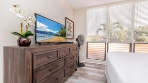 A bedroom with a bed, a dresser, a television, and a window with blinds. - Breath taking views, secluded sandy beach, oceanfront luxury (Lahaina)