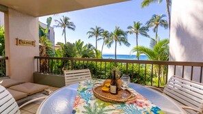 A balcony with a table set for two, a bottle of wine, and a tropical-themed tablecloth. - Breath taking views, secluded sandy beach, oceanfront luxury (Lahaina)