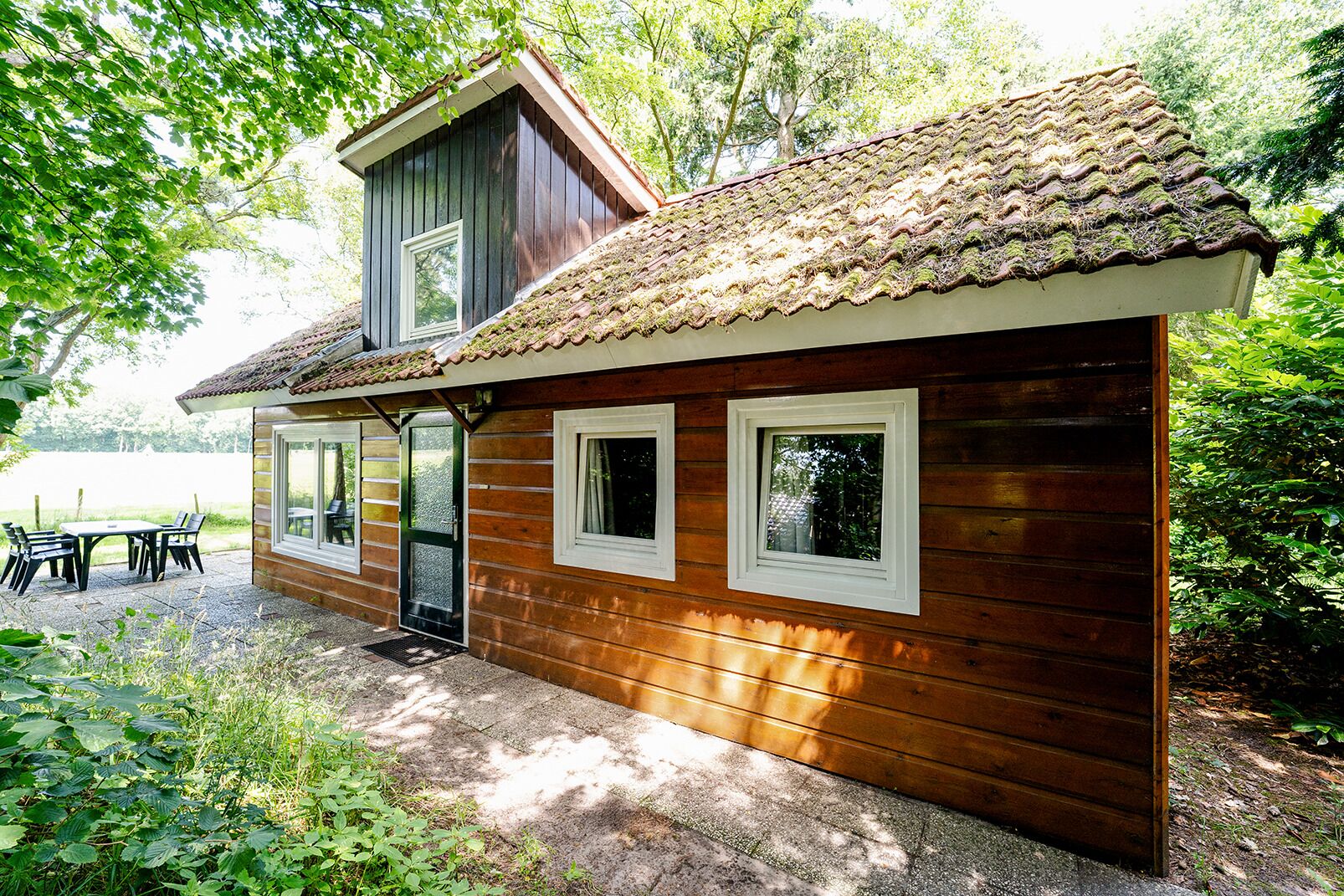 A wooden cabin with a tiled roof, a balcony, and a patio with outdoor seating.
