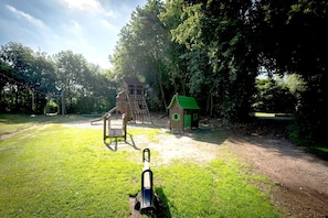 Une aire de jeux avec un toboggan, des structures d’escalade et une petite maison de jeux dotée d’un toit végétalisé.