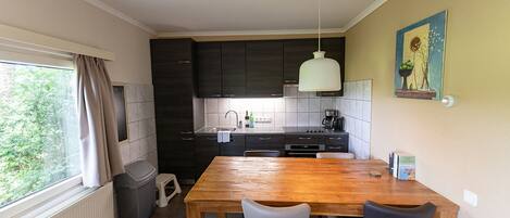 Eine kompakte Küche mit dunklen Schränken, einem Holztisch und einer Pendelleuchte.