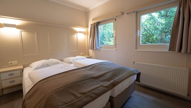 Een hotelkamer met een bed, nachtkastjes, een raam met gordijnen en een radiator.
